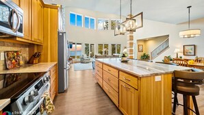 A spacious kitchen with wooden cabinets, a large island, and a view of the outdoors. - Northern Door County Waterfront Home (Sturgeon Bay)