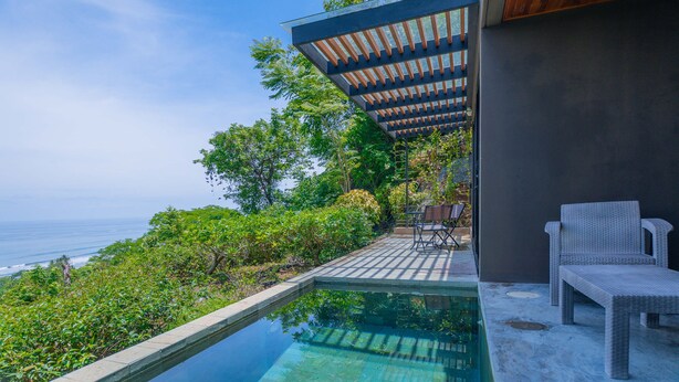 Ein Poolbereich mit Meerblick, einer Pergola und Gartenmöbeln.