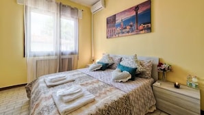 A hotel room with a bed, a nightstand, a painting on the wall, and a window with curtains. - Venice Miramare Residence 2 (Mestre)