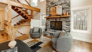 A spacious living room with a stone fireplace, a wooden staircase, and a large window. - Beautiful Home in Stone Ridge (Stone Ridge)