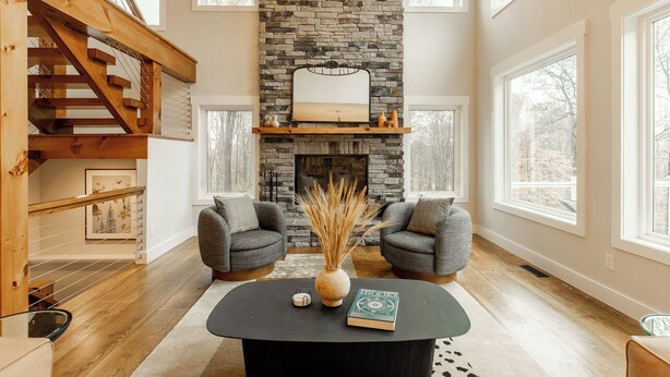 A spacious living room with a stone fireplace, two gray armchairs, a black coffee table, and a wooden staircase. - Beautiful Home in Stone Ridge (Stone Ridge)
