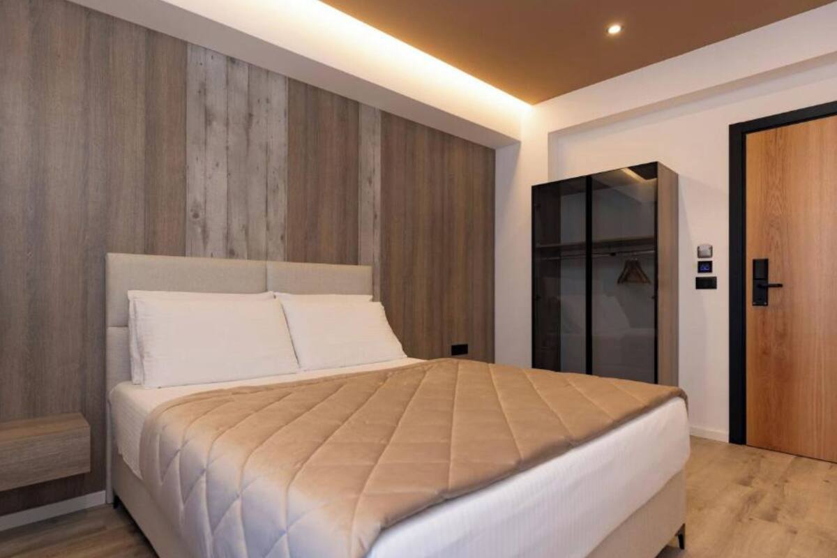 A modern bedroom with a bed, wooden panel wall, and a wardrobe.