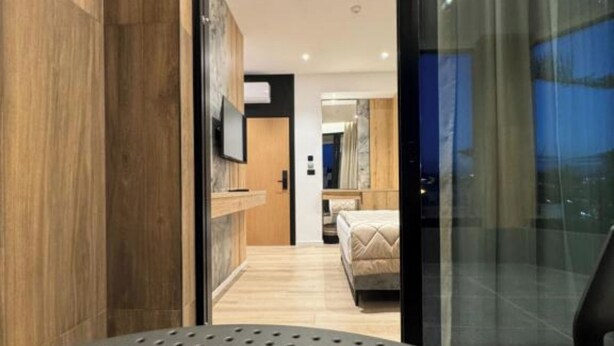 Una habitación de hotel moderna con una pared de acento de madera, una cama con edredón color beige y un espejo grande.