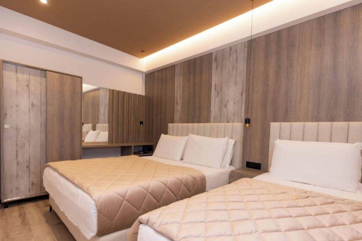 A modern hotel room with two beds, wooden panel walls, and a large mirror.