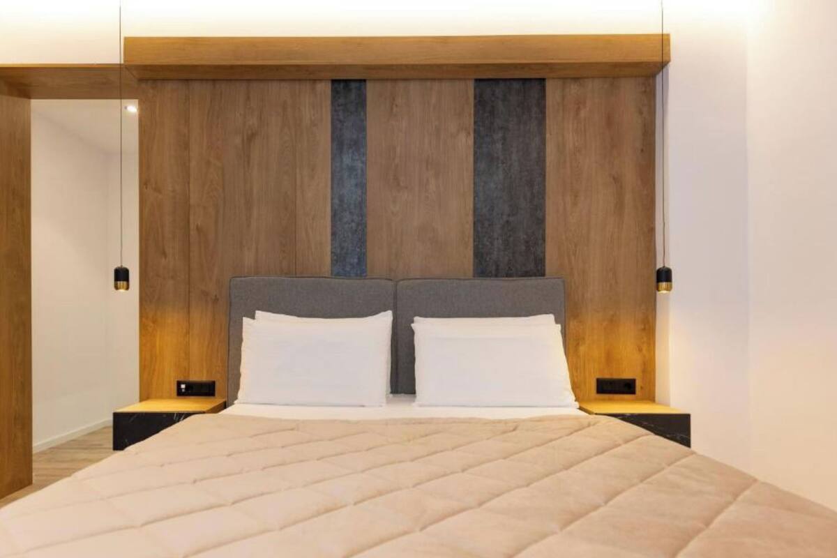 A double bed with a quilted cover, two bedside tables with lamps, and a wooden headboard with vertical accents.