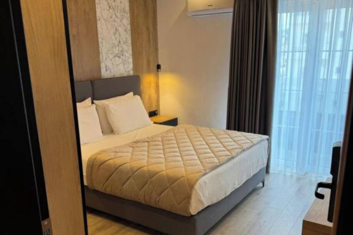 A neatly made bed with a quilted cover, a bedside table with a lamp, and a window with curtains.