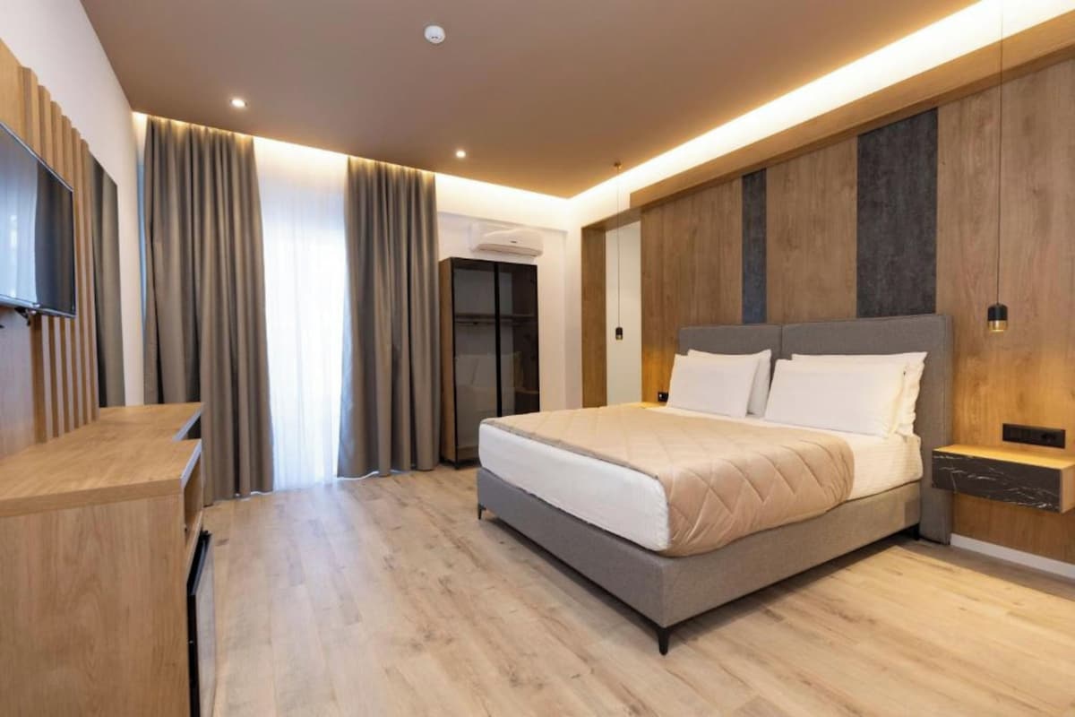 Un dormitorio moderno con una cama grande, paneles de madera, televisión integrada y un escritorio.