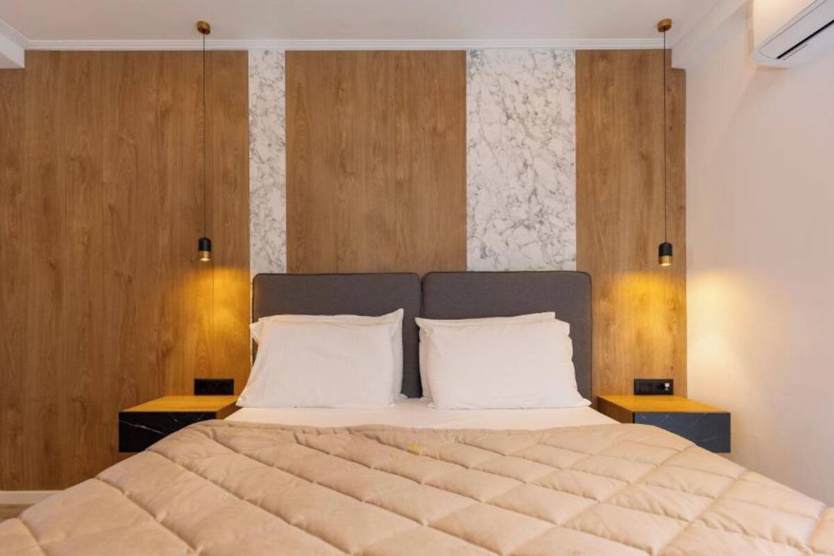 A modern bedroom with a large bed, wooden panel wall, marble accents, and bedside lamps.