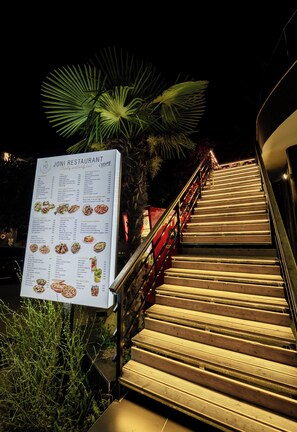 A restaurant menu board with a staircase leading to the entrance. - Hotel Joni (Ksamil)