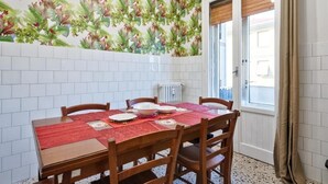 Un comedor con una mesa lista para cuatro personas, rodeada de sillas de madera, un mantel rojo y un papel tapiz estampado.