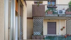 Un balcón estrecho con puerta de vidrio, barandilla metálica y una pequeña zona cubierta por un toldo verde.