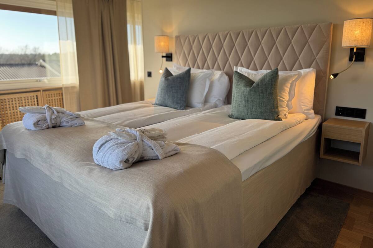 Une chambre d’hôtel avec un grand lit, deux tables de chevet, une tête de lit et une fenêtre avec des rideaux.