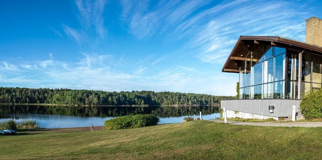 A modern building with large glass windows overlooking a lake and forest.
