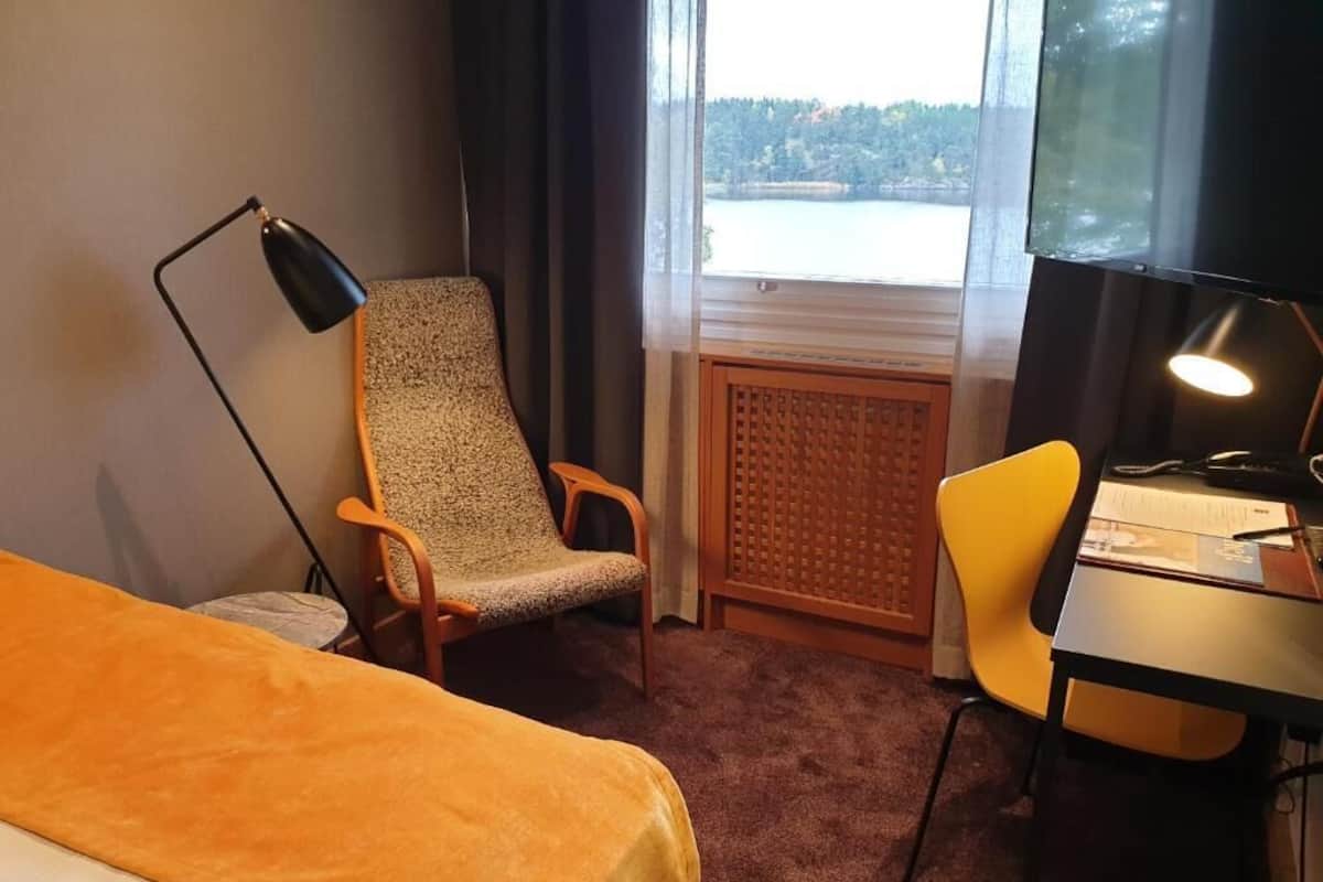 Une chambre d’hôtel comprenant un lit, un bureau, une chaise, un lampadaire et une vue sur un lac par la fenêtre.