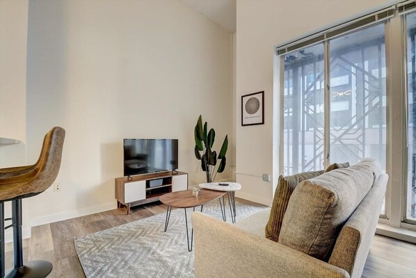 Relax in this stylish living room with a large window offering a view of the city, a flat-screen TV, and a comfortable sofa.