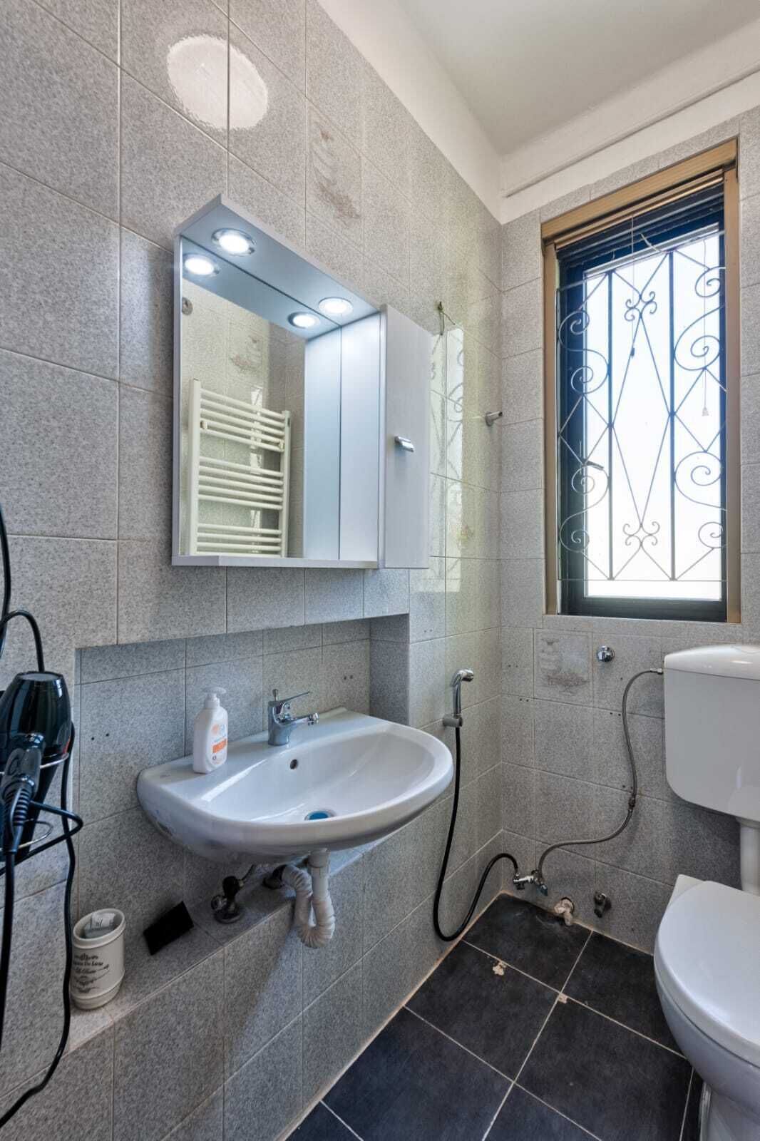 Ein Badezimmer mit weißem Waschbecken, einem Spiegel, einem Fenster mit Verzierungen und einer Toilette.