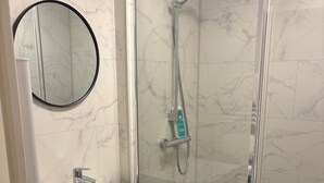 Une salle de bain avec un lavabo blanc, un meuble-vasque noir, un miroir rond et une douche en verre avec un pommeau de douche à main.