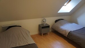 Une chambre avec deux lits, une table de chevet avec un miroir et une lucarne.