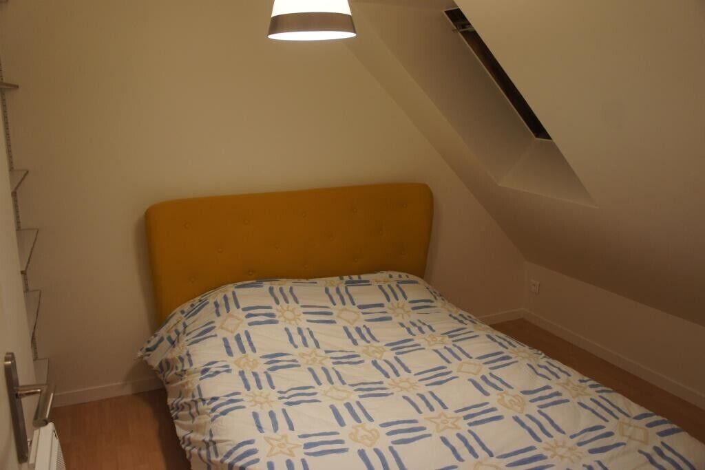 A small, single-bed room with a yellow headboard and a patterned bedspread.