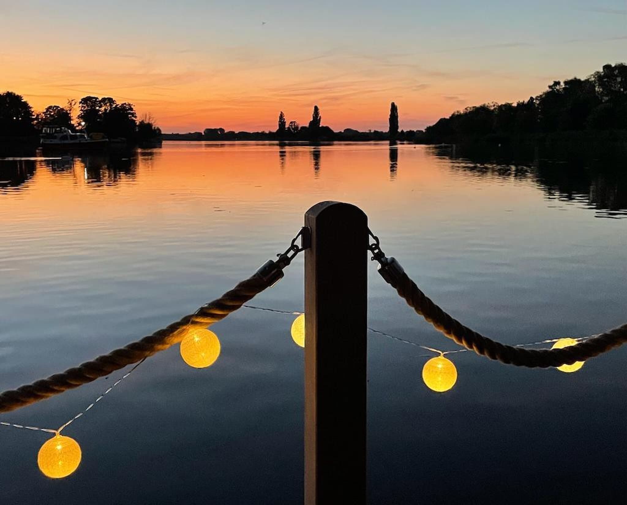 Una barriera di corde con luci, una superficie d'acqua calma e un cielo al tramonto.
