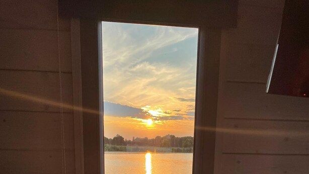 Uitzicht door een raam van een houten hutje met een meer en een zonsondergang.