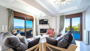 A modern living room with a fireplace, a television, and a view of the outdoors. - Karyo Villa,- 4bd, 3min On Foot From The Beach! (Pirgos)