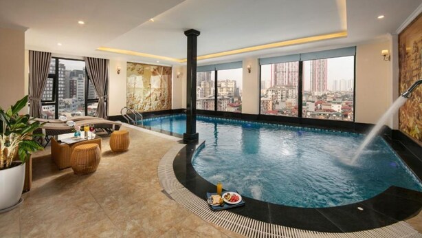 Ein Rooftop-Pool mit unendlicher Optik und Blick auf die Stadt, eine Liege sowie ein Essbereich mit Tisch für zwei Personen.