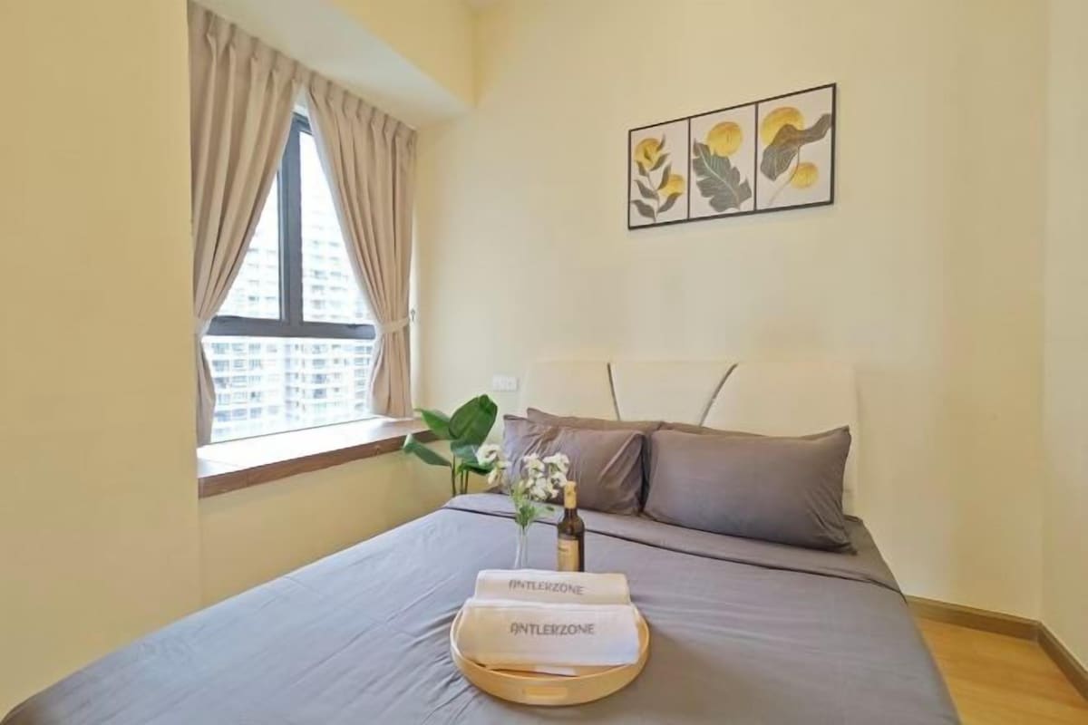 Habitación de hotel con cama, ventana con cortinas, una planta y una bandeja con botella y vasos.