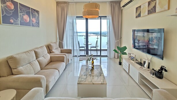 Una sala de estar moderna con un sofá, una mesa de centro y un televisor. Hay un balcón con vistas al mar.