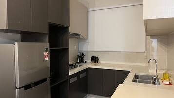 A modern kitchen with dark cabinets, a stainless steel refrigerator, a sink, and a countertop with a kettle and utensils.
