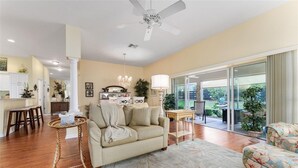 A spacious living room with a beige sofa, a round coffee table, and a large window offering a view of the outdoors.