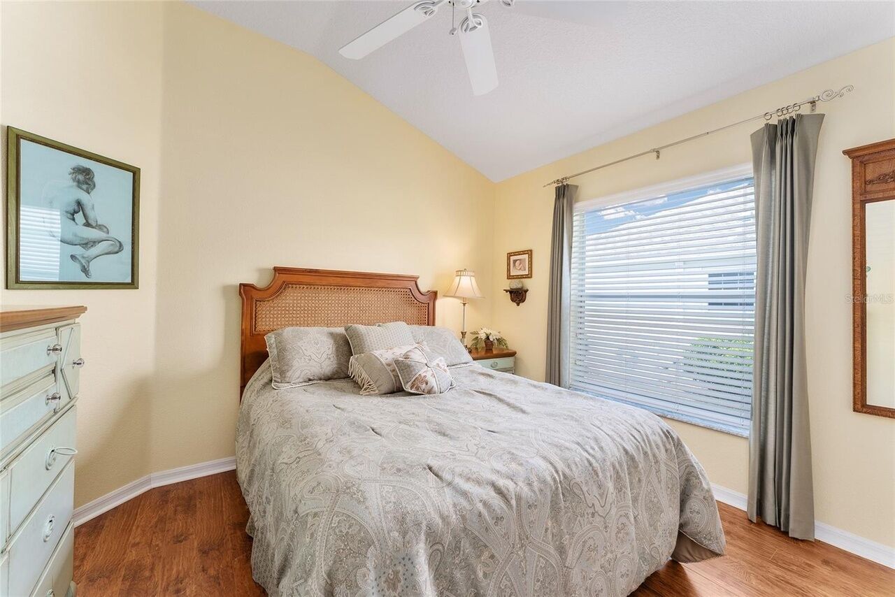 Un dormitorio con cama, cómoda, ventilador de techo, ventana con persianas e imagen enmarcada en la pared.