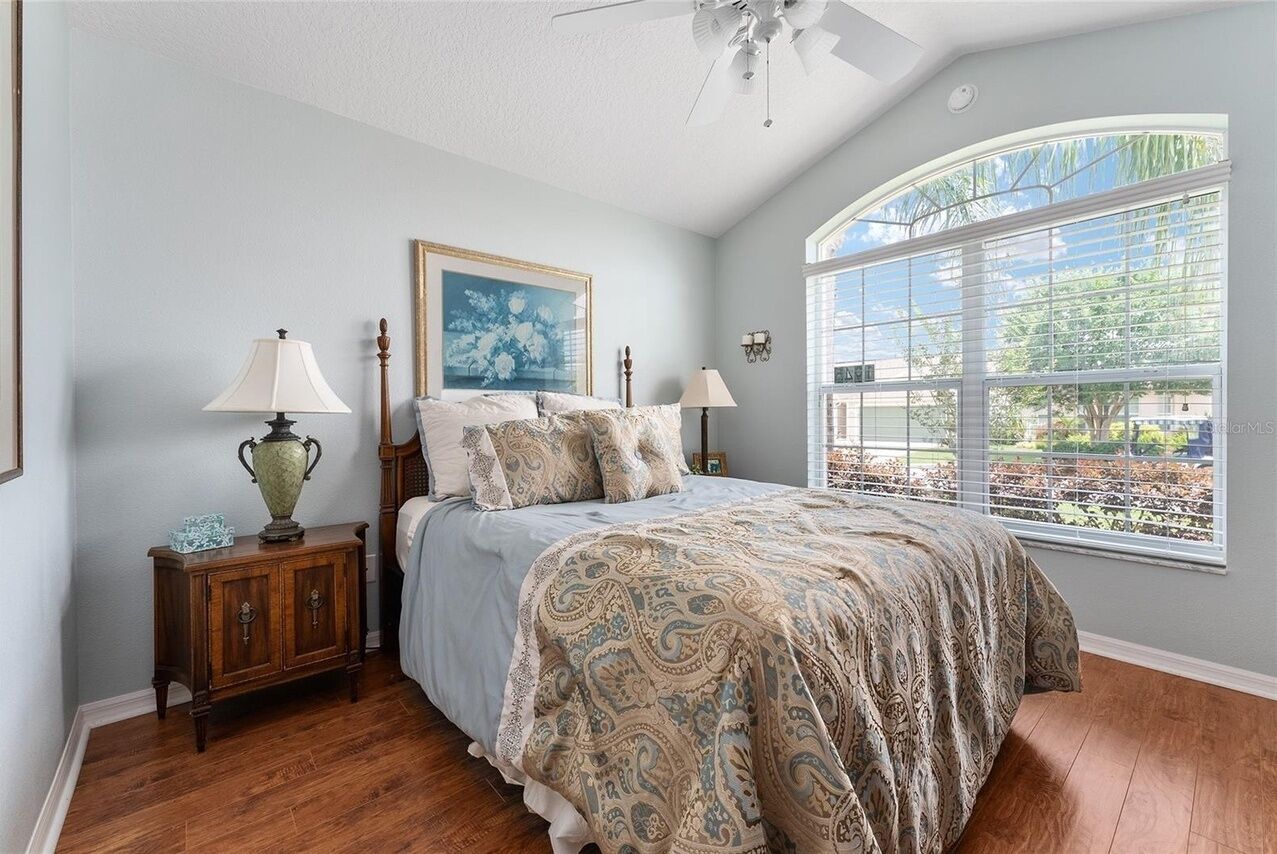 A bedroom with a bed, nightstands, a ceiling fan, a large window, and a framed picture on the wall.