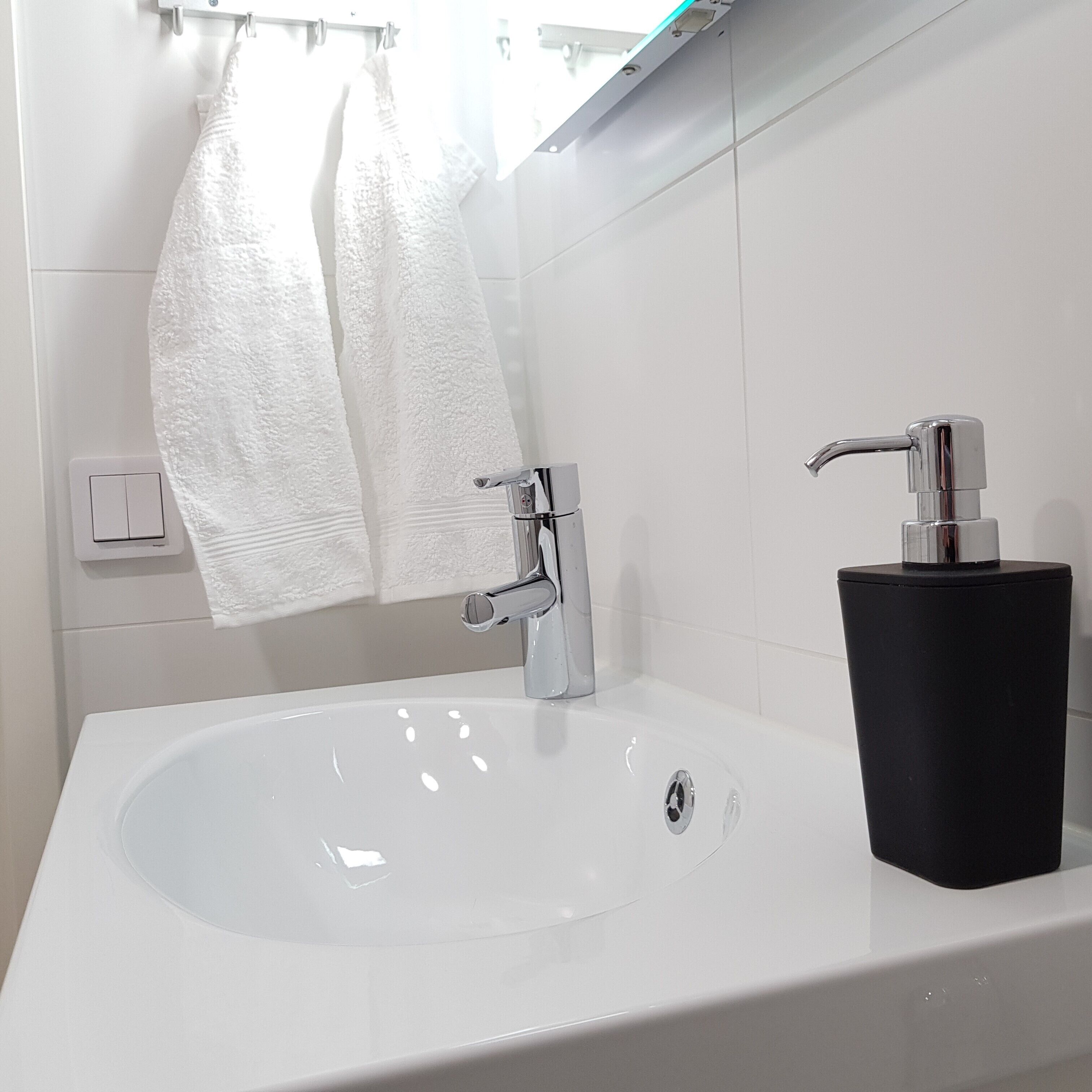 Ein Badezimmer mit einem weißen Waschbecken, einem chromfarbenen Wasserhahn und einem schwarzen Seifenspender.