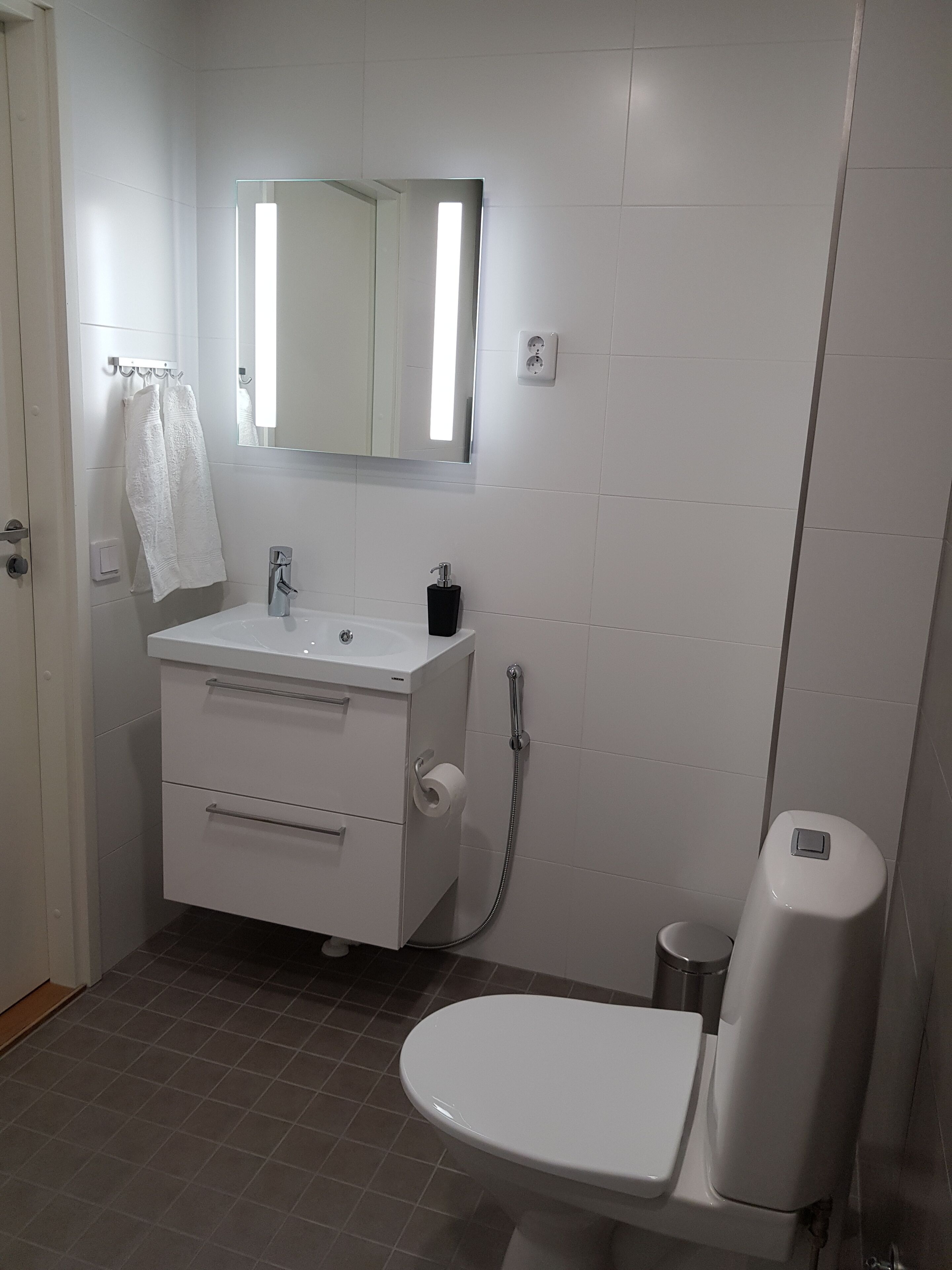 Un baño con lavamanos, espejo e inodoro blancos.