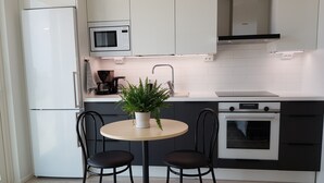 Une cuisine moderne avec des meubles blancs, un four à micro-ondes, une machine à café et une plante en pot sur une table ronde accompagnée de deux chaises.