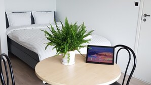 Une chambre moderne avec un lit, une table ronde et deux chaises, une plante en pot et une tablette posée sur la table.