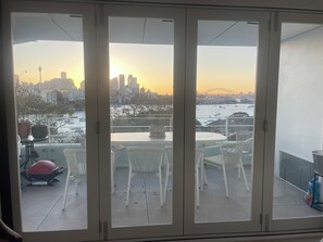Ein Balkon mit Tisch und Stühlen, mit Blick auf eine Stadtlandschaft mit einer Brücke und Gebäuden.