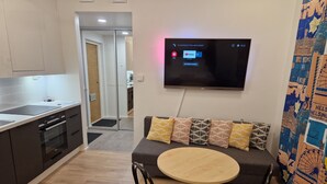 A modern kitchen with a dining area, a flat-screen TV mounted on the wall, and a sofa with patterned cushions. - Cozy corner next to the Mall of Tripla (Helsinki)