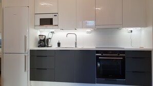 A modern kitchen with white and dark grey cabinetry, a built-in microwave, a coffee maker, and an oven. - Cozy corner next to the Mall of Tripla (Helsinki)
