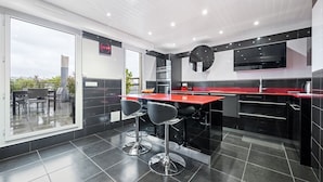 Una cocina moderna con encimeras negras y rojas, electrodomésticos de acero inoxidable y un televisor grande montado en la pared.