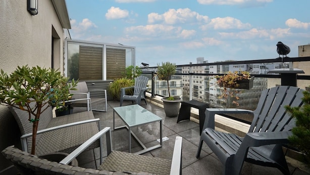 Una terraza en la azotea con mobiliario exterior, plantas en macetas y vistas de la ciudad.