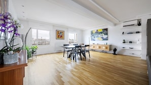 Amplia sala de estar con piso de madera, una mesa de comedor con sillas y vistas a la ciudad a través de amplios ventanales.