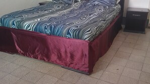 Ein Bett mit einem gemusterten Überwurf, einem roten Bettrock und zwei Nachttischen mit Schubladen.