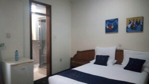Ein Hotelzimmer mit einem Bett, einem kleinen Schreibtisch, einem Spiegel und einer Tür zu einem Badezimmer. An der Wand hängen zwei Bilder.