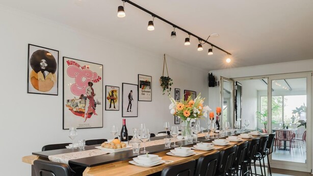 A dining area with a long table set for a meal, framed artwork on the walls, and a view through the glass door. - Amsterdam Group Villa | 20+ | Spa | Karaoke (Zwanenburg)
