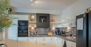 A modern kitchen with white cabinets, a Bosch oven, a coffee machine, and a black backsplash. - Amsterdam Group Villa | 16+ beds | 4 - 5 bedrooms (Zwanenburg)