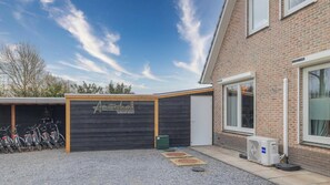 A building with a brick facade, a wooden sign reading 'Amsterdam Group Stay,' and a bicycle parking area. - Amsterdam Group Villa | 16+ beds | 4 - 5 bedrooms (Zwanenburg)