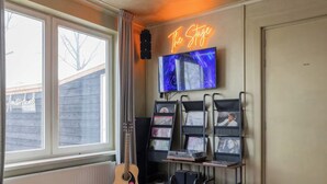 A room with a large window, a neon sign reading 'The Stage,' a television, and a guitar. - Amsterdam Group Villa | 20+ | Spa | Karaoke (Zwanenburg)