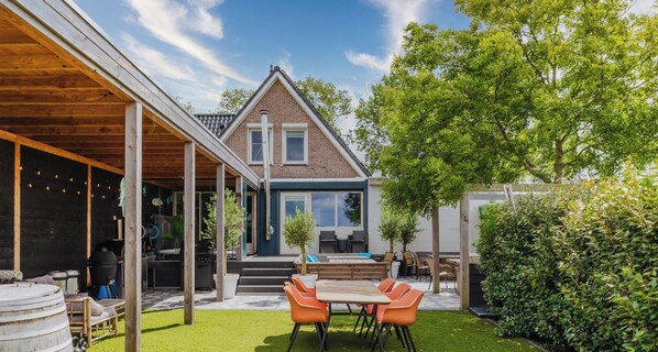 A modern house with a covered patio, outdoor seating, and a well-maintained lawn. - Amsterdam Group Villa | 16+ beds | 4 - 5 bedrooms (Zwanenburg)